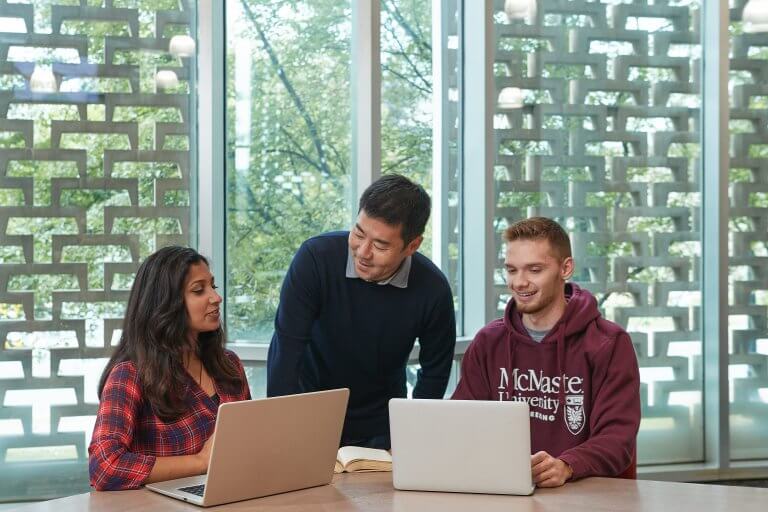 Three students talking and working over their laptops at a table